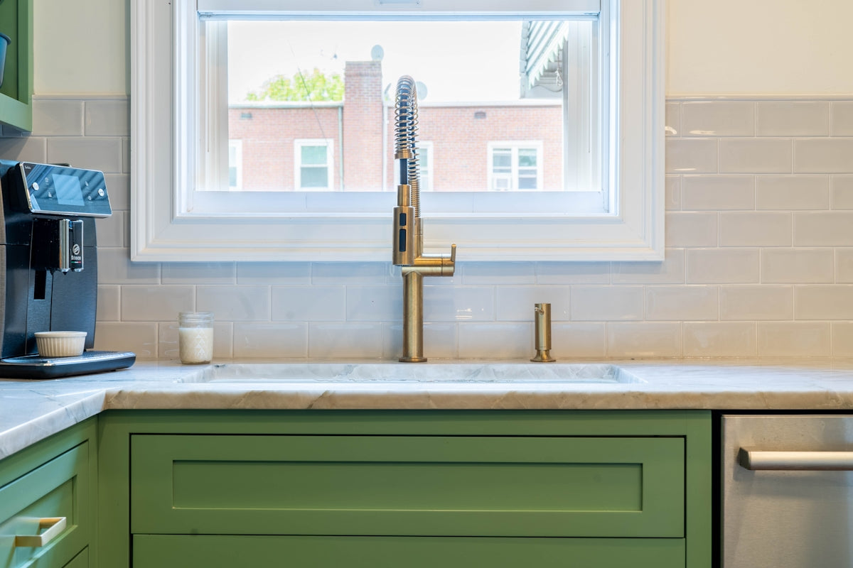 a kitchen with green cabinets and a gold faucet