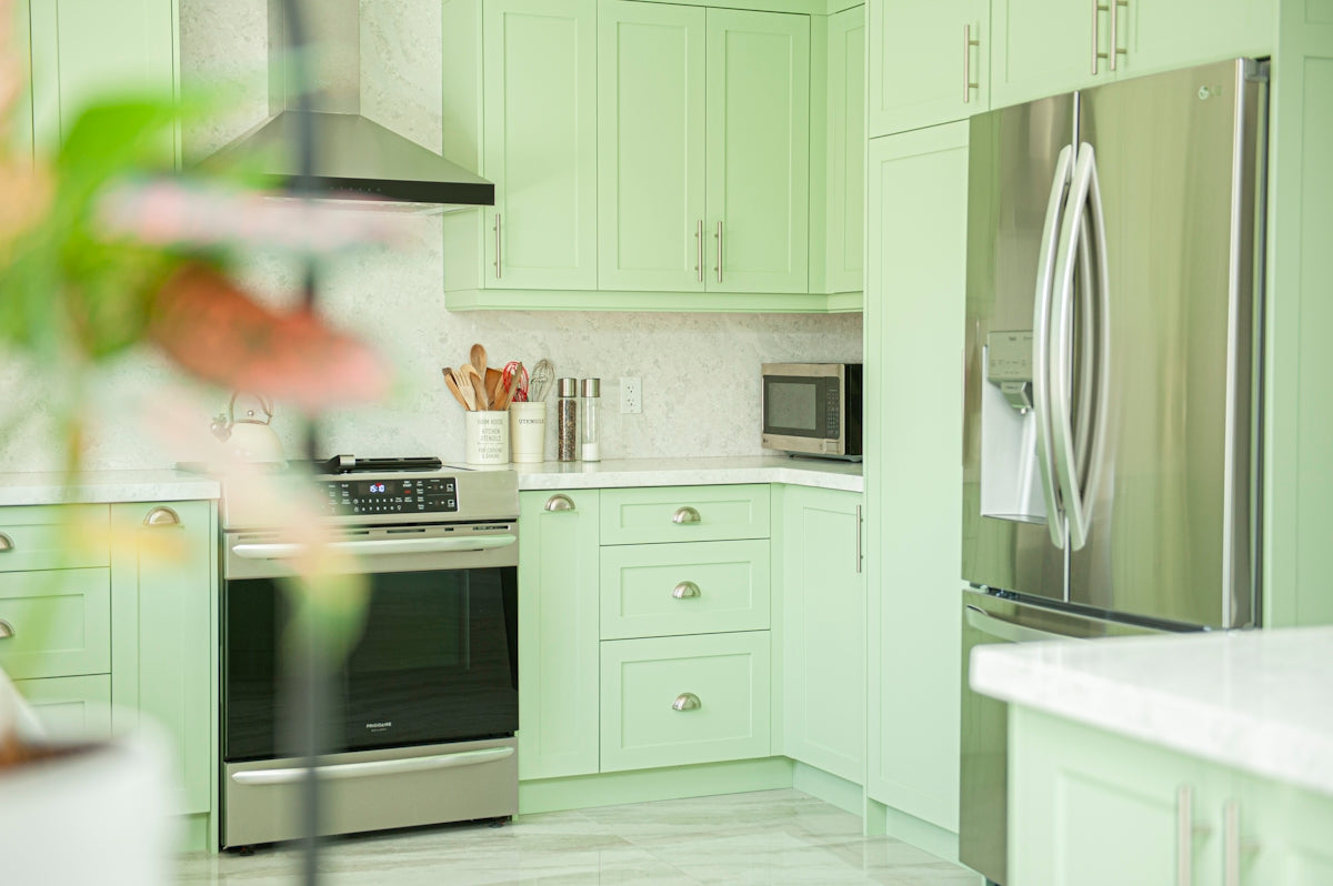 Modern kitchen with light green cabinets and stainless steel appliances.